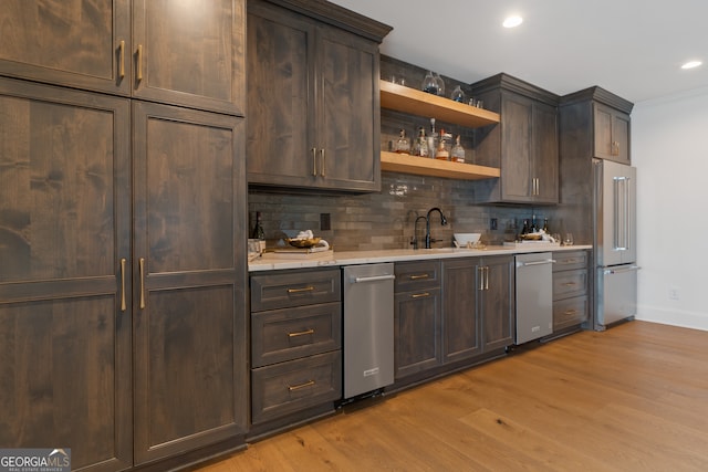 kitchen featuring sink, tasteful backsplash, dark brown cabinets, light hardwood / wood-style flooring, and appliances with stainless steel finishes