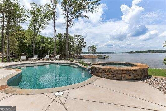 view of pool with a patio, a water view, and an in ground hot tub