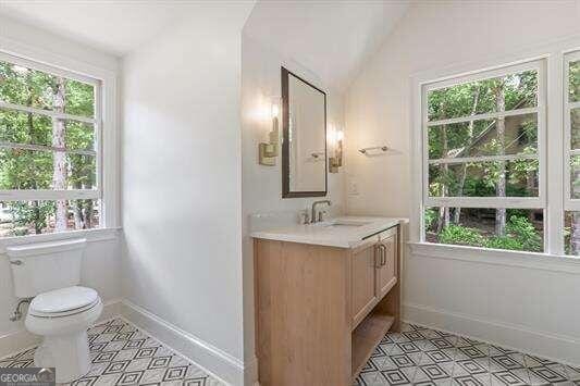 bathroom featuring a healthy amount of sunlight, lofted ceiling, vanity, and toilet