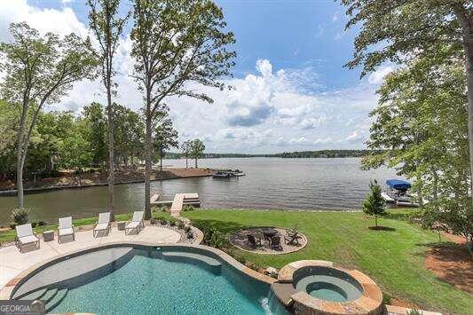 view of pool with a yard, an in ground hot tub, a water view, and a patio area