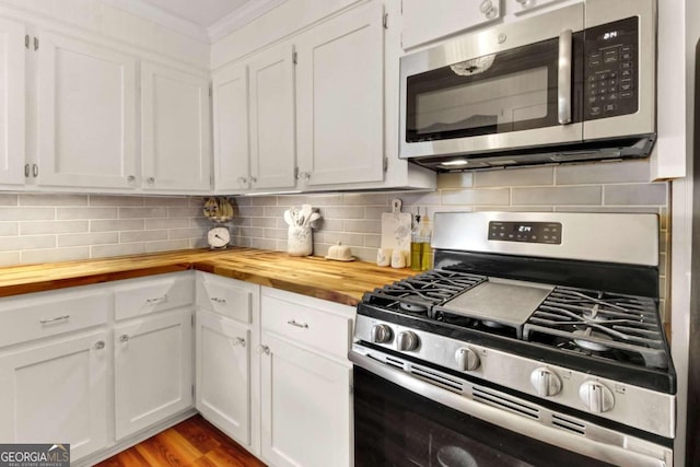 kitchen featuring butcher block countertops, crown molding, appliances with stainless steel finishes, decorative backsplash, and white cabinets