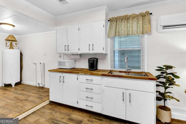 kitchen with an AC wall unit, dark hardwood / wood-style floors, white cabinetry, sink, and ornamental molding