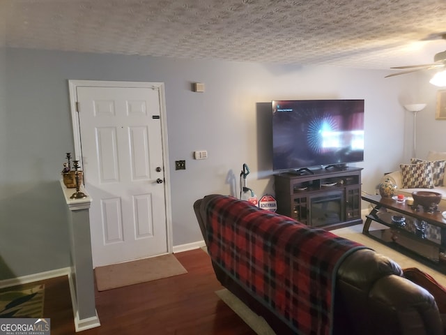 living room with a ceiling fan, a textured ceiling, baseboards, and wood finished floors