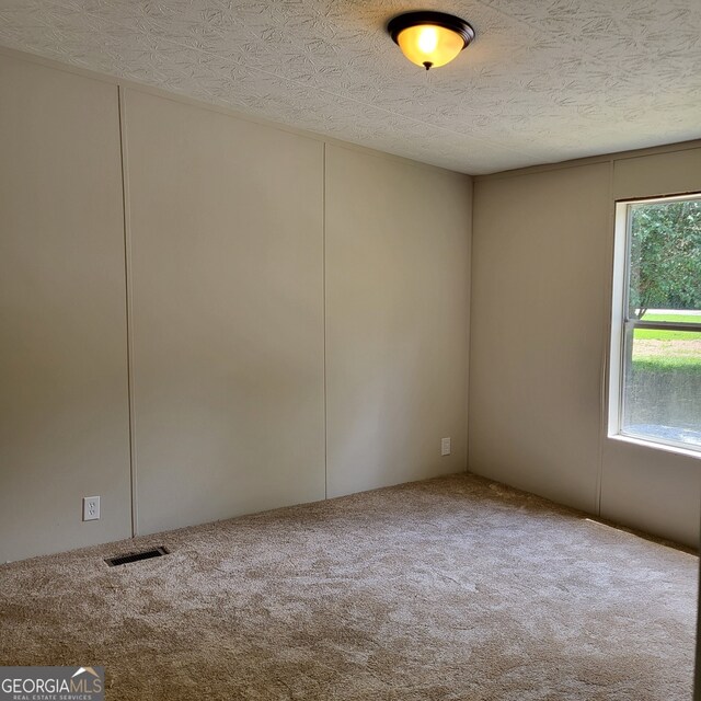 empty room with carpet, visible vents, and a textured ceiling