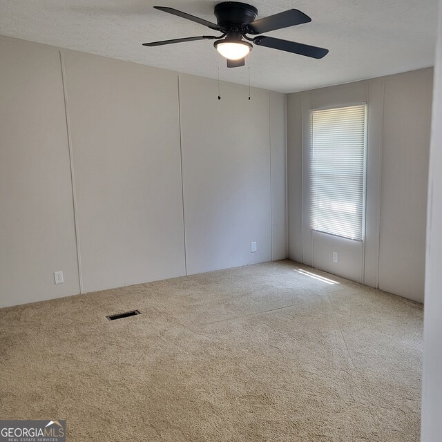 unfurnished room with a textured ceiling, carpet, visible vents, and a ceiling fan