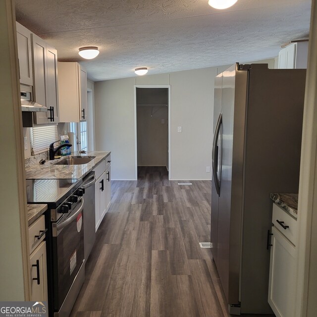 kitchen with stone counters, white cabinetry, appliances with stainless steel finishes, and a sink