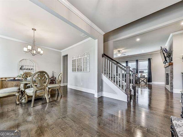 dining area featuring dark wood-type flooring, ornamental molding, a brick fireplace, and ceiling fan with notable chandelier