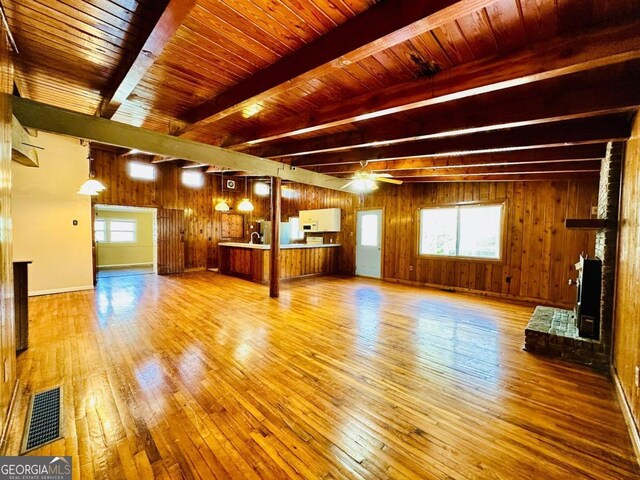 unfurnished living room with beamed ceiling, wood walls, and light hardwood / wood-style floors