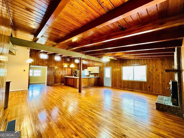 unfurnished living room with beamed ceiling, wooden walls, and light hardwood / wood-style floors