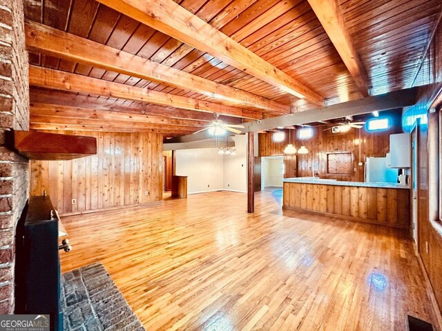 unfurnished living room with beam ceiling, wood walls, light wood-type flooring, and ceiling fan