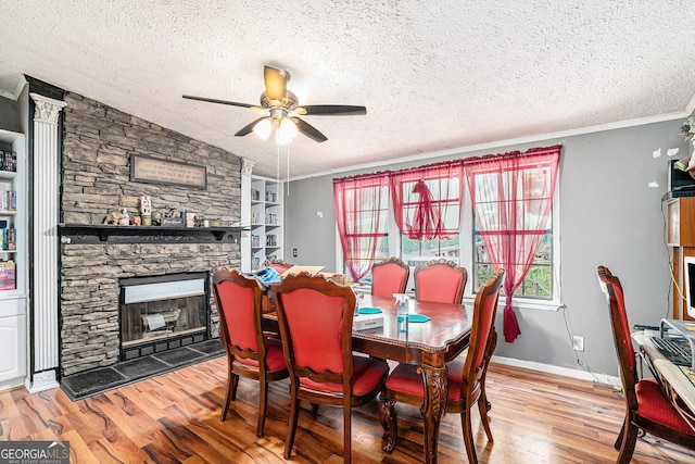 dining area with a stone fireplace, wood-type flooring, ornamental molding, ceiling fan, and a textured ceiling