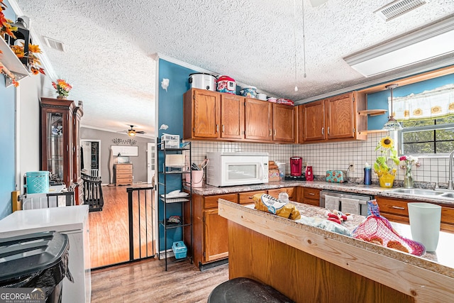 kitchen featuring sink, light hardwood / wood-style flooring, backsplash, a textured ceiling, and stainless steel dishwasher