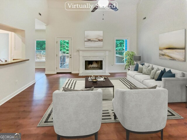 living room with dark wood-type flooring, ceiling fan, a high ceiling, and a high end fireplace