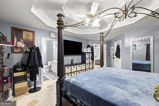 bedroom with ceiling fan, a tray ceiling, ornamental molding, and ensuite bath