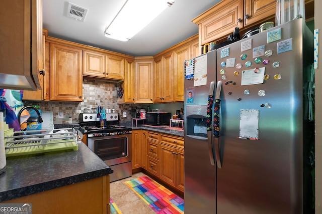 kitchen with brown cabinetry, visible vents, dark countertops, stainless steel appliances, and backsplash