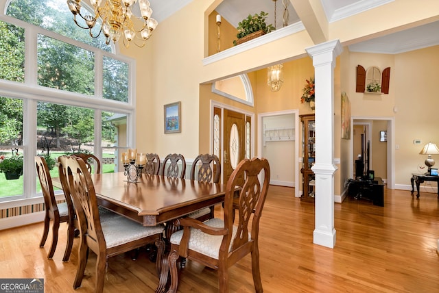 dining space featuring an inviting chandelier, decorative columns, light wood-type flooring, ornamental molding, and a towering ceiling