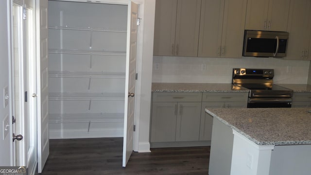 interior space with appliances with stainless steel finishes, gray cabinetry, dark hardwood / wood-style flooring, decorative backsplash, and light stone counters