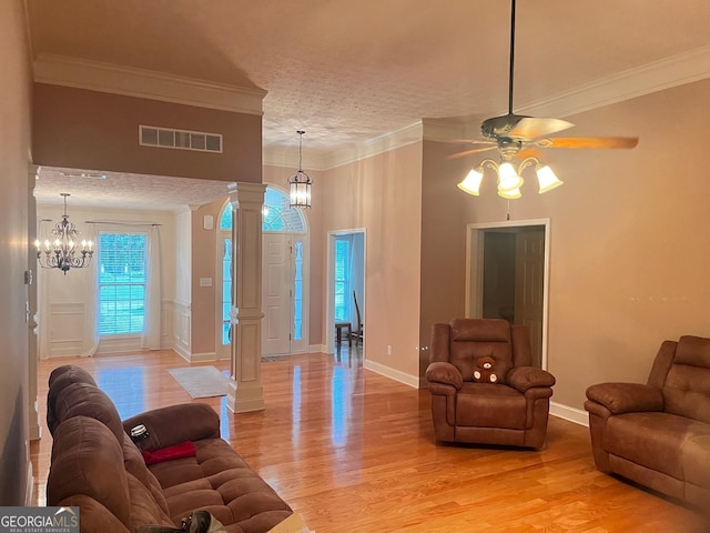 living room with ornate columns, ornamental molding, a textured ceiling, ceiling fan with notable chandelier, and light wood-type flooring