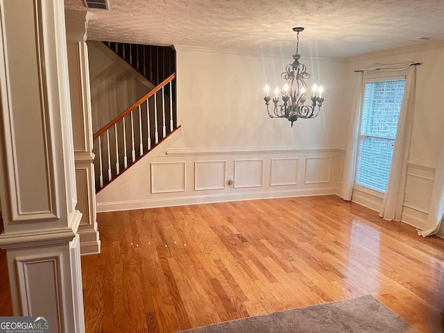 unfurnished dining area with crown molding, a notable chandelier, a textured ceiling, and light wood-type flooring