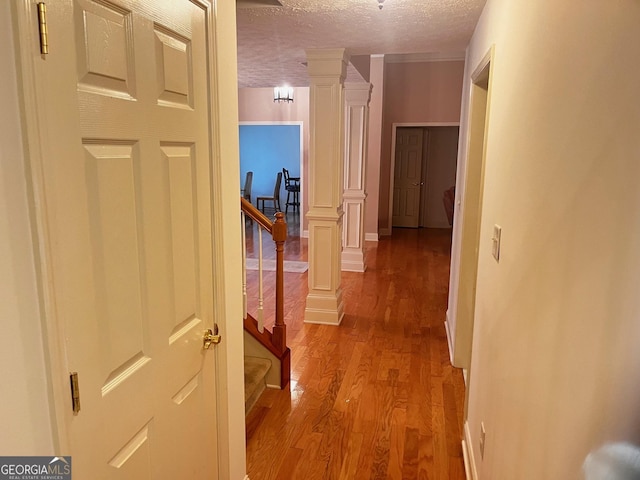 hall featuring a textured ceiling, light hardwood / wood-style flooring, and ornate columns