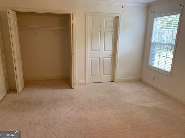 unfurnished bedroom featuring ornamental molding, light colored carpet, and a closet