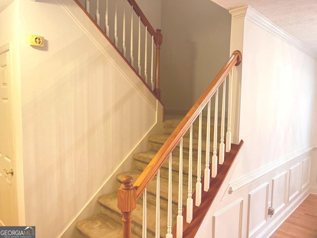 stairs featuring wood-type flooring, ornamental molding, and a textured ceiling