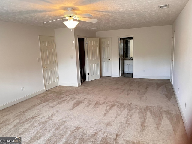 interior space with ceiling fan, ensuite bath, carpet flooring, and a textured ceiling