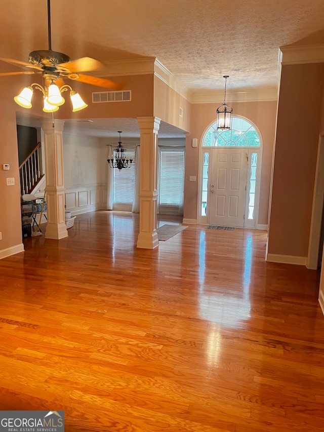 foyer with light hardwood / wood-style flooring, crown molding, a textured ceiling, ceiling fan with notable chandelier, and ornate columns