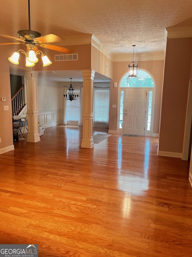 entrance foyer featuring ornate columns, a textured ceiling, light wood-type flooring, ornamental molding, and ceiling fan with notable chandelier