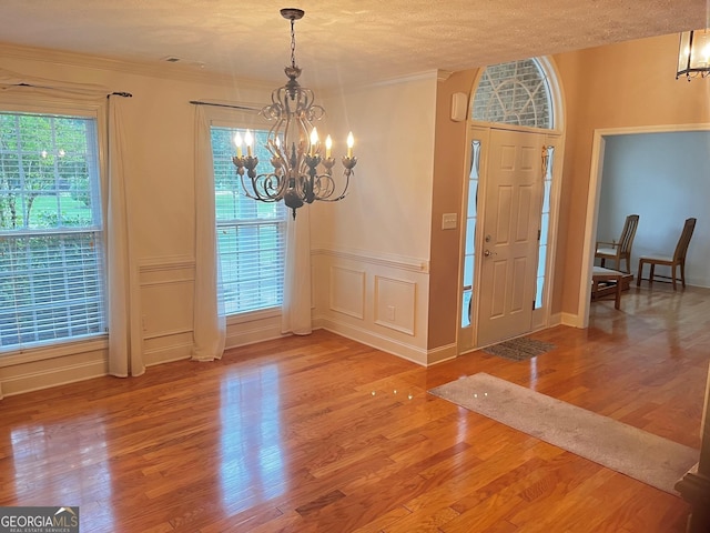 foyer with hardwood / wood-style flooring, ornamental molding, a textured ceiling, and a notable chandelier