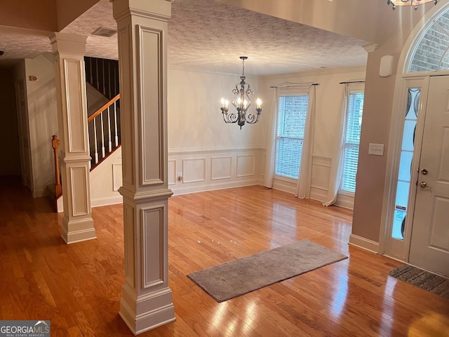 foyer entrance featuring a chandelier, a textured ceiling, ornamental molding, hardwood / wood-style flooring, and decorative columns