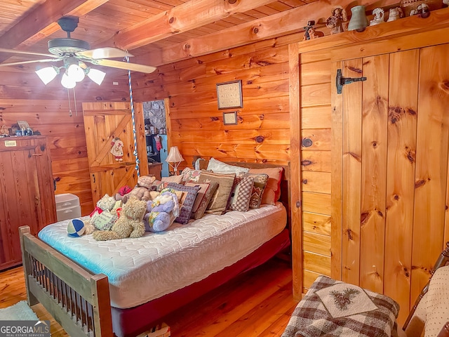 bedroom featuring beamed ceiling, wooden walls, hardwood / wood-style flooring, wooden ceiling, and ceiling fan