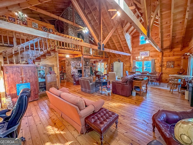living area with wood walls, stairway, beam ceiling, hardwood / wood-style flooring, and a ceiling fan