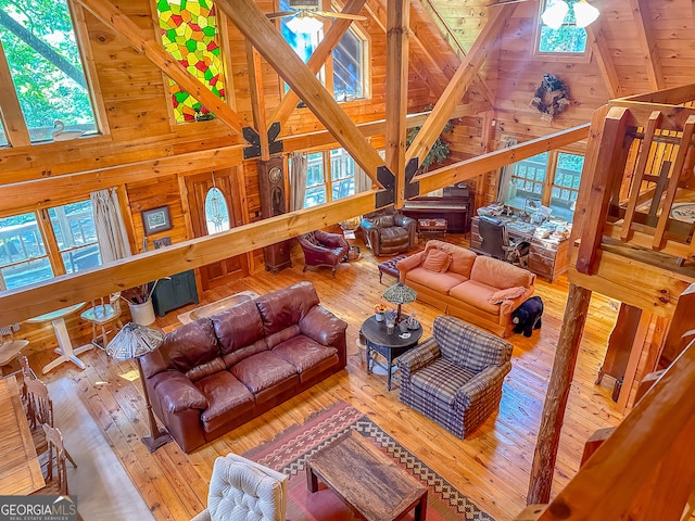 living room featuring wood walls, high vaulted ceiling, ceiling fan, and light wood-type flooring