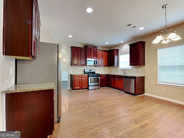 kitchen featuring sink, an inviting chandelier, hanging light fixtures, stainless steel appliances, and light stone countertops