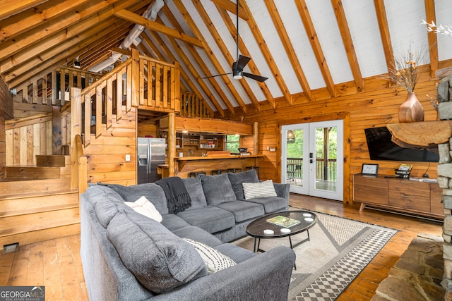 living room with french doors, wooden walls, light wood-type flooring, beamed ceiling, and high vaulted ceiling