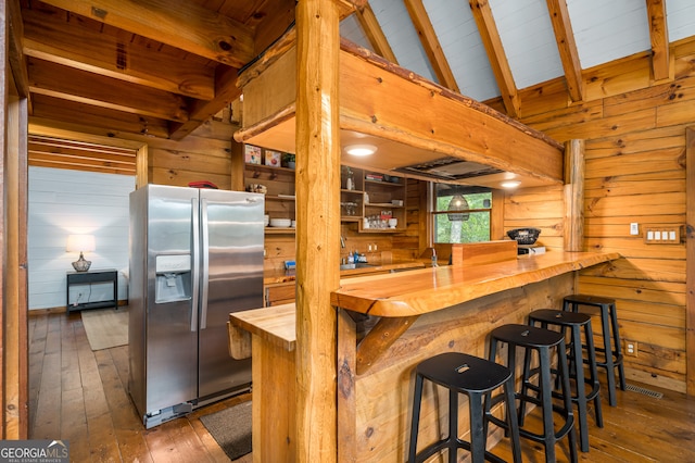 kitchen with stainless steel fridge with ice dispenser, wooden walls, wood counters, dark hardwood / wood-style floors, and vaulted ceiling with skylight