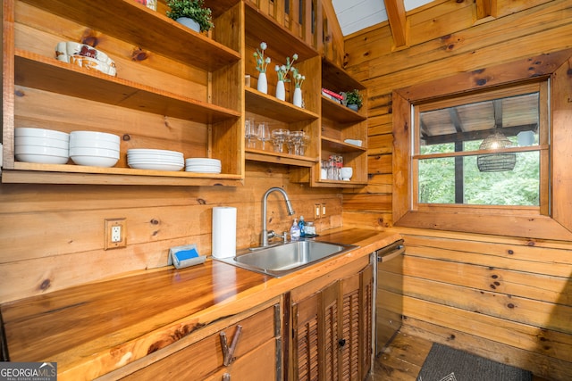 kitchen featuring wooden walls, hardwood / wood-style floors, wooden counters, sink, and stainless steel dishwasher