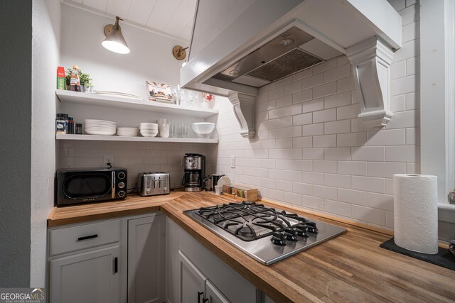 kitchen featuring premium range hood, butcher block counters, decorative backsplash, hardwood / wood-style floors, and stainless steel gas cooktop