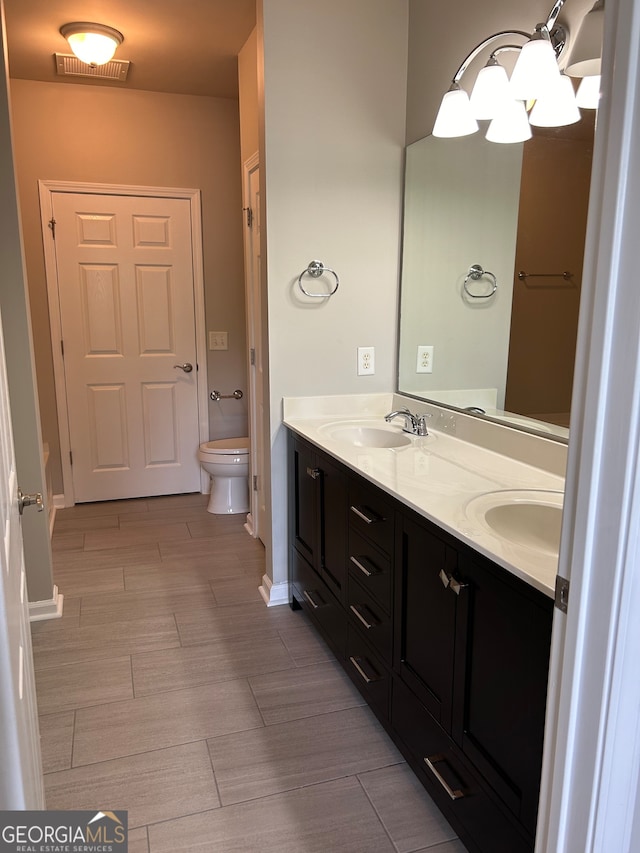 bathroom with toilet, double sink vanity, and tile patterned floors