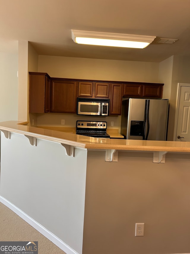 kitchen featuring appliances with stainless steel finishes, carpet, a kitchen bar, and kitchen peninsula