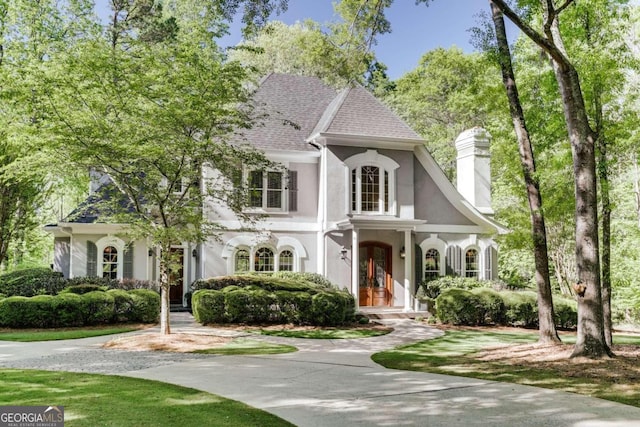 view of front facade with driveway, a shingled roof, a chimney, and stucco siding