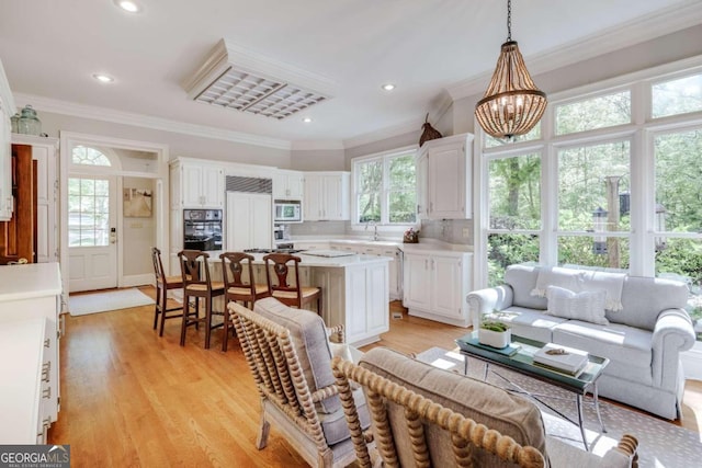 living room with light wood-type flooring, crown molding, recessed lighting, and an inviting chandelier