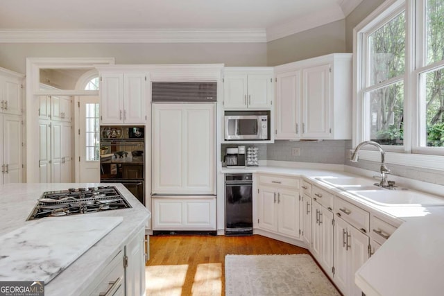 kitchen with light hardwood / wood-style flooring, white cabinets, built in appliances, sink, and ornamental molding