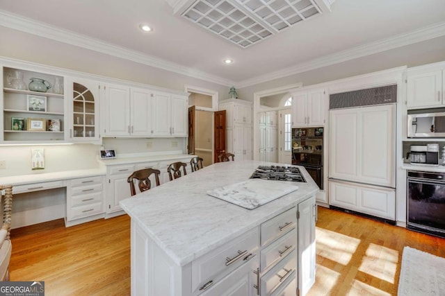 kitchen with light wood finished floors, built in desk, appliances with stainless steel finishes, and white cabinetry