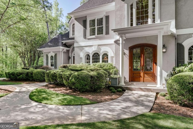 view of exterior entry featuring french doors, roof with shingles, and stucco siding