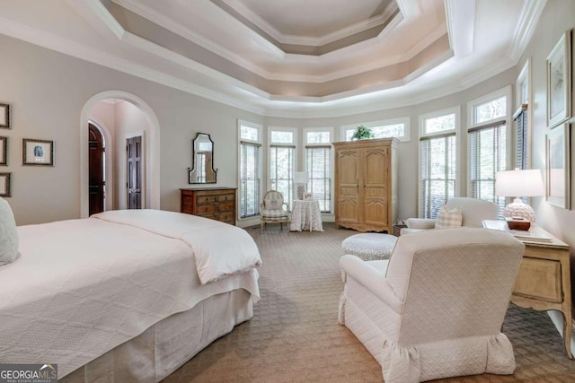 carpeted bedroom with arched walkways, ornamental molding, a raised ceiling, and a walk in closet