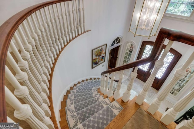 staircase with a high ceiling, arched walkways, a chandelier, and wood finished floors