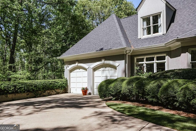 view of property exterior featuring a garage, a shingled roof, concrete driveway, and stucco siding