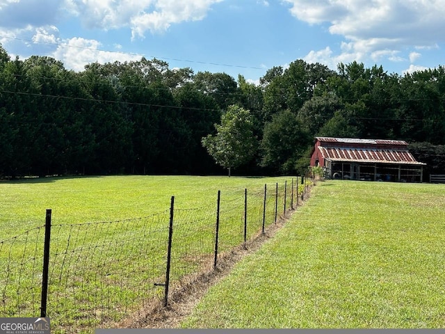 view of yard with fence, an outdoor structure, a wooded view, and a rural view